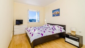 A bedroom with a bed, a TV on a dresser, a window with a view, and a painting on the wall. - Niko's Sea View Apartment (Dubrovnik)