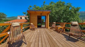 A wooden deck with lounge chairs and a small wooden structure with glass doors.