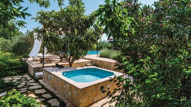 A rectangular pool with stone walls, surrounded by lush greenery and a clear blue sky.