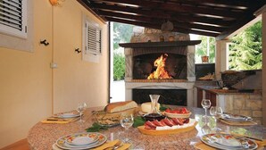An outdoor dining area with a stone fireplace, a round table set for four, and a grill in the background.