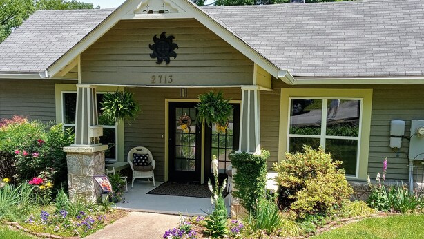 Una casa con il numero 2713 sulla facciata, un portico con una sedia e un giardino curato.