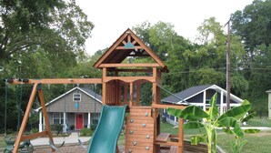 Un’area giochi in legno con scivolo, altalene e strutture per arrampicata.
