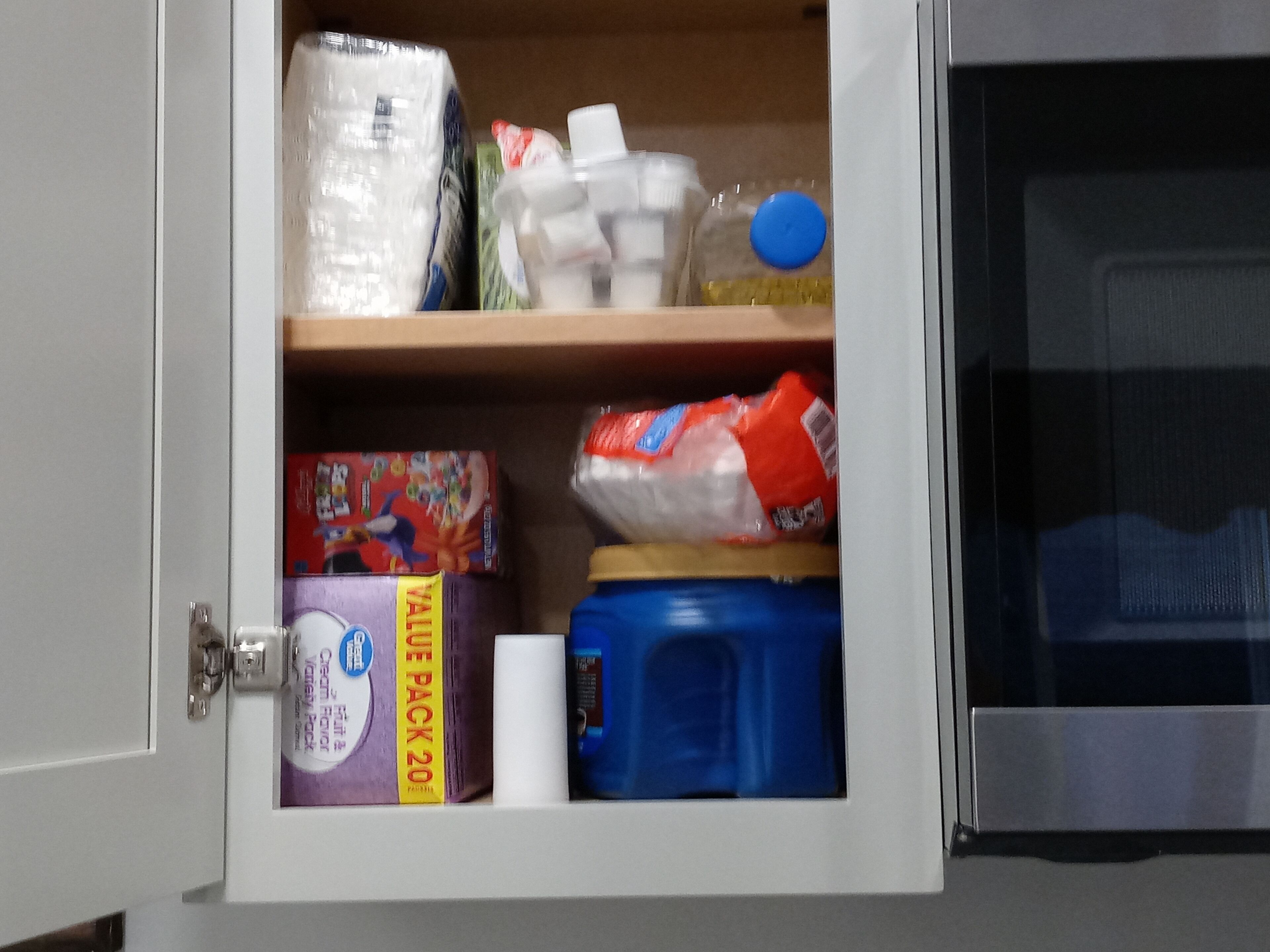 A kitchen cabinet with various items including a pack of tissues, a blue container, and a box of ValVue Pack 20.