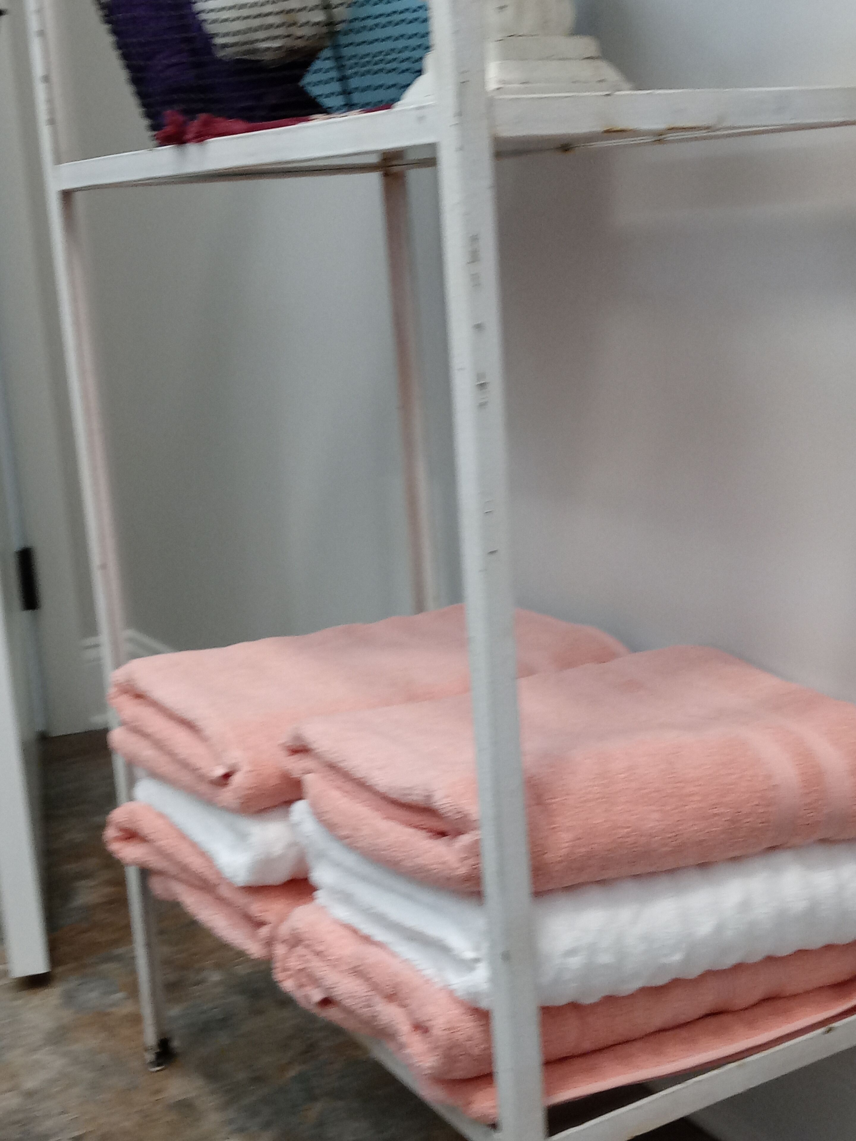 Een metalen plank met opgevouwen handdoeken in roze- en witte tinten.