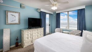 Una habitación de hotel con una cama grande, un televisor en una cómoda, un balcón con vistas y un ventilador de techo.