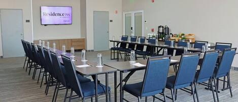 Un salón de conferencias con una larga mesa, sillas, una pantalla de televisión y una estación de café.