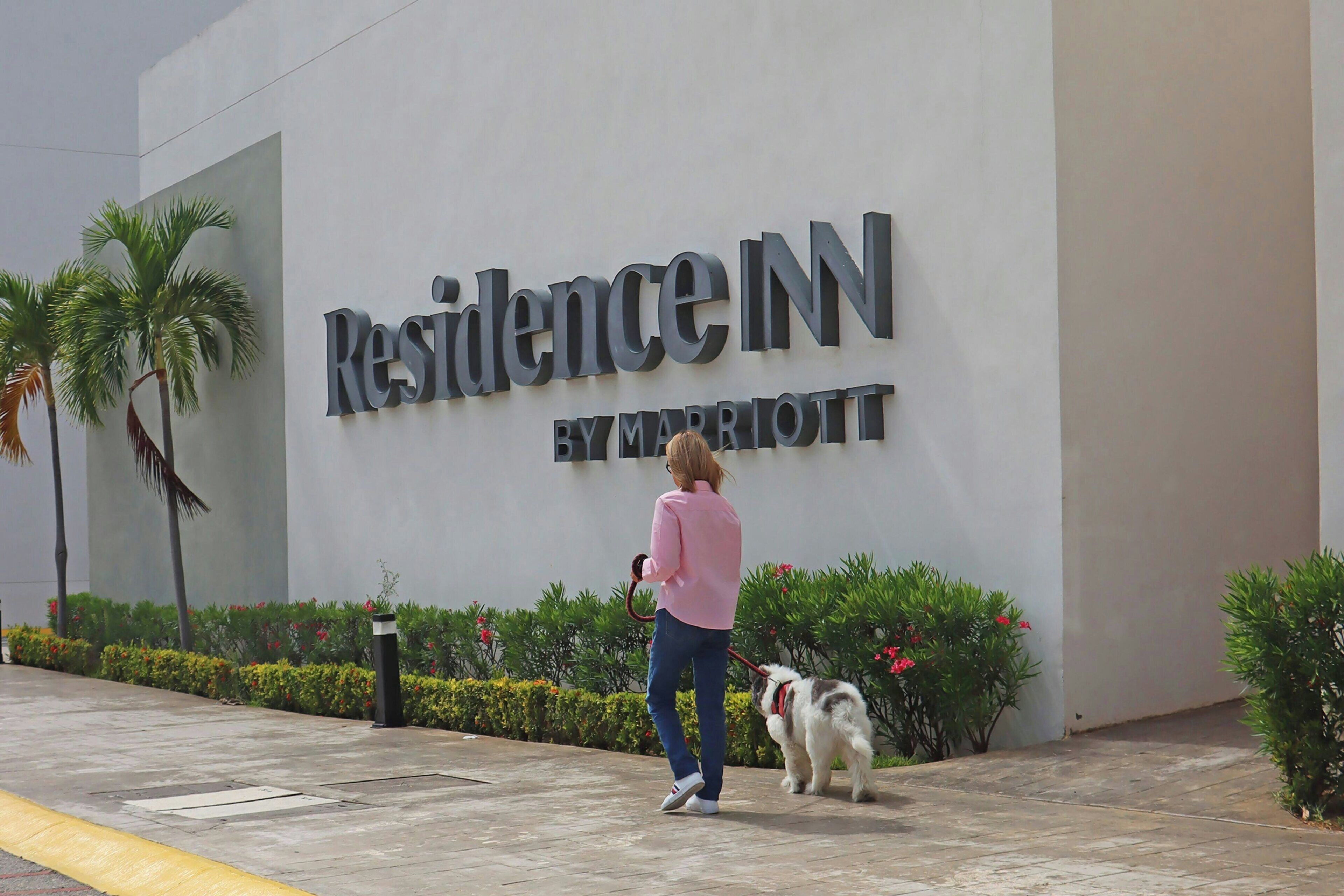 Una persona pasea un perro frente a un edificio con un cartel que dice 'Residence Inn by Marriott'.