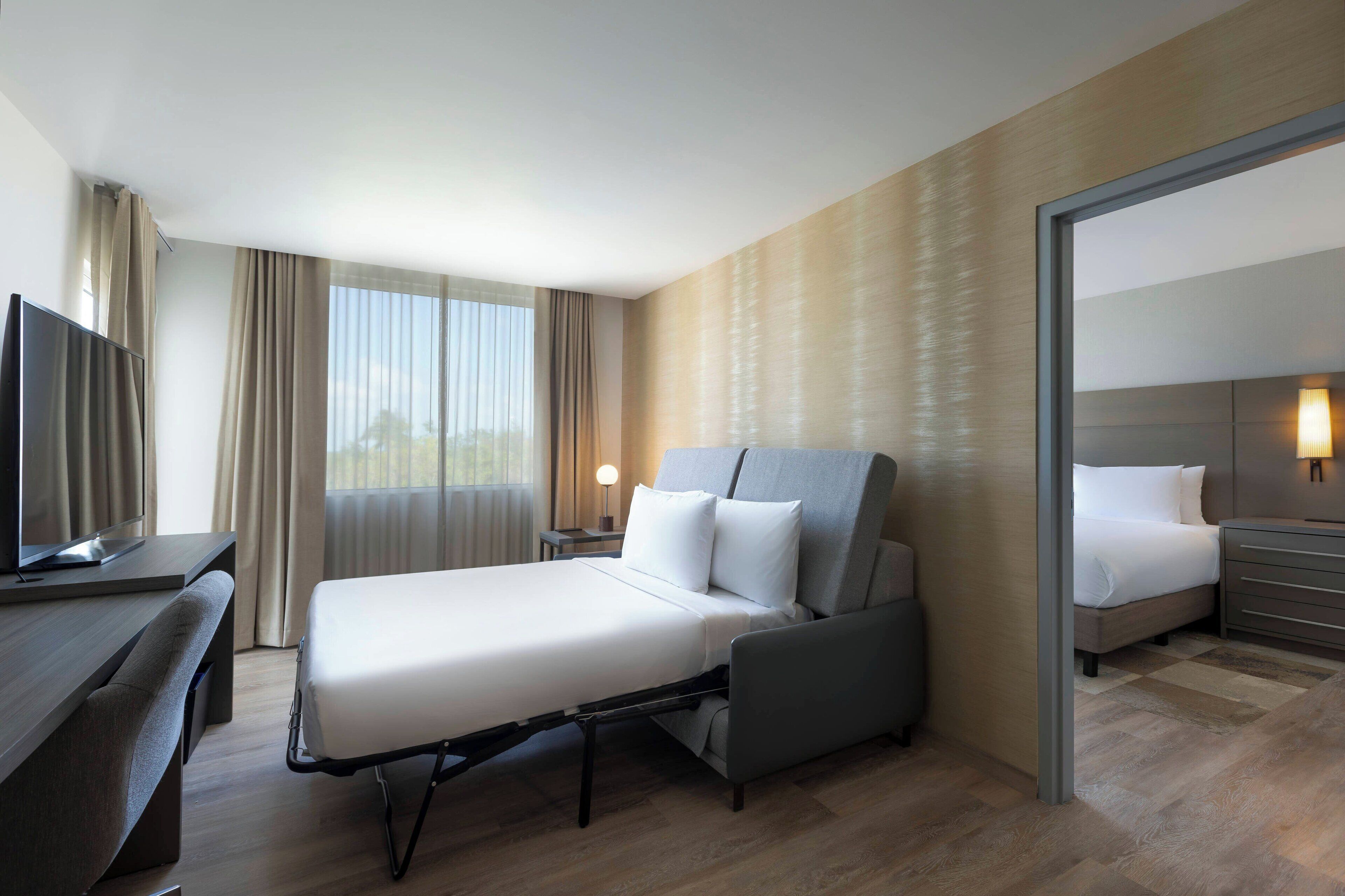 Une chambre d’hôtel moderne équipée d’un lit, d’un bureau, d’une télévision et d’un grand miroir.