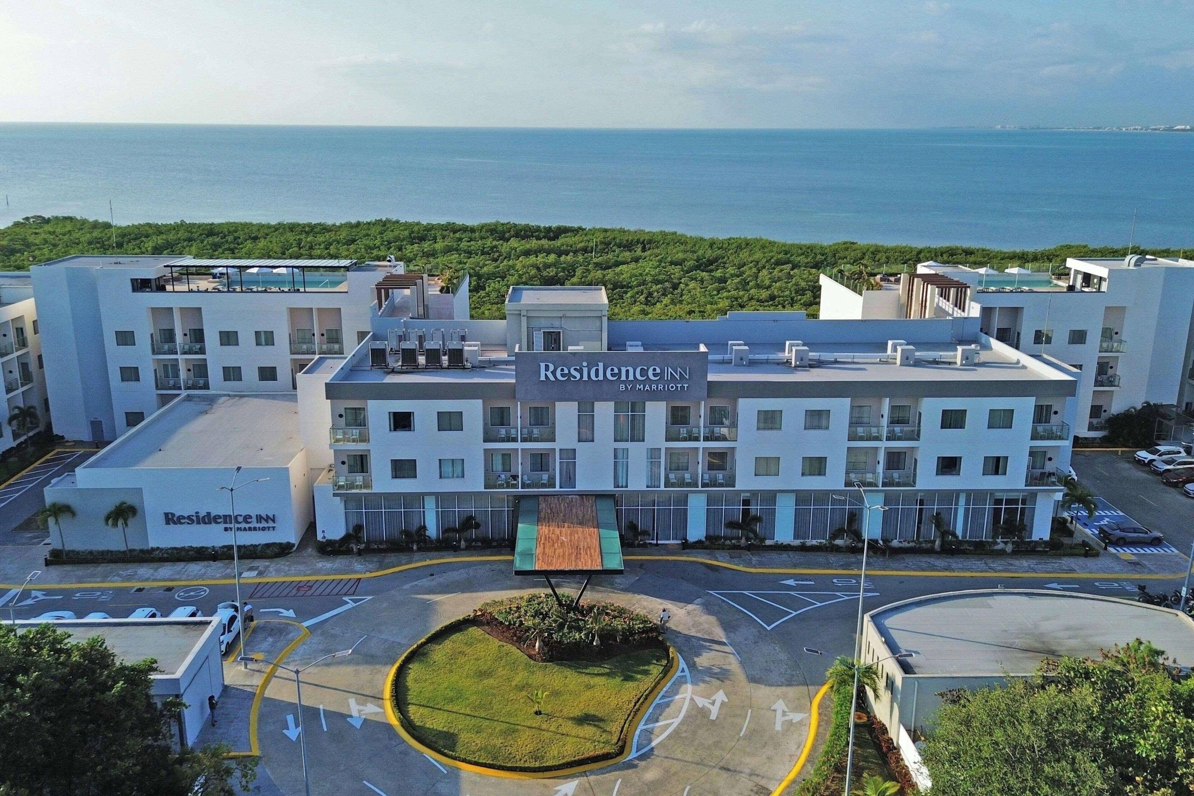 A multi-story hotel with a rooftop pool, a parking lot, and a view of the sea.