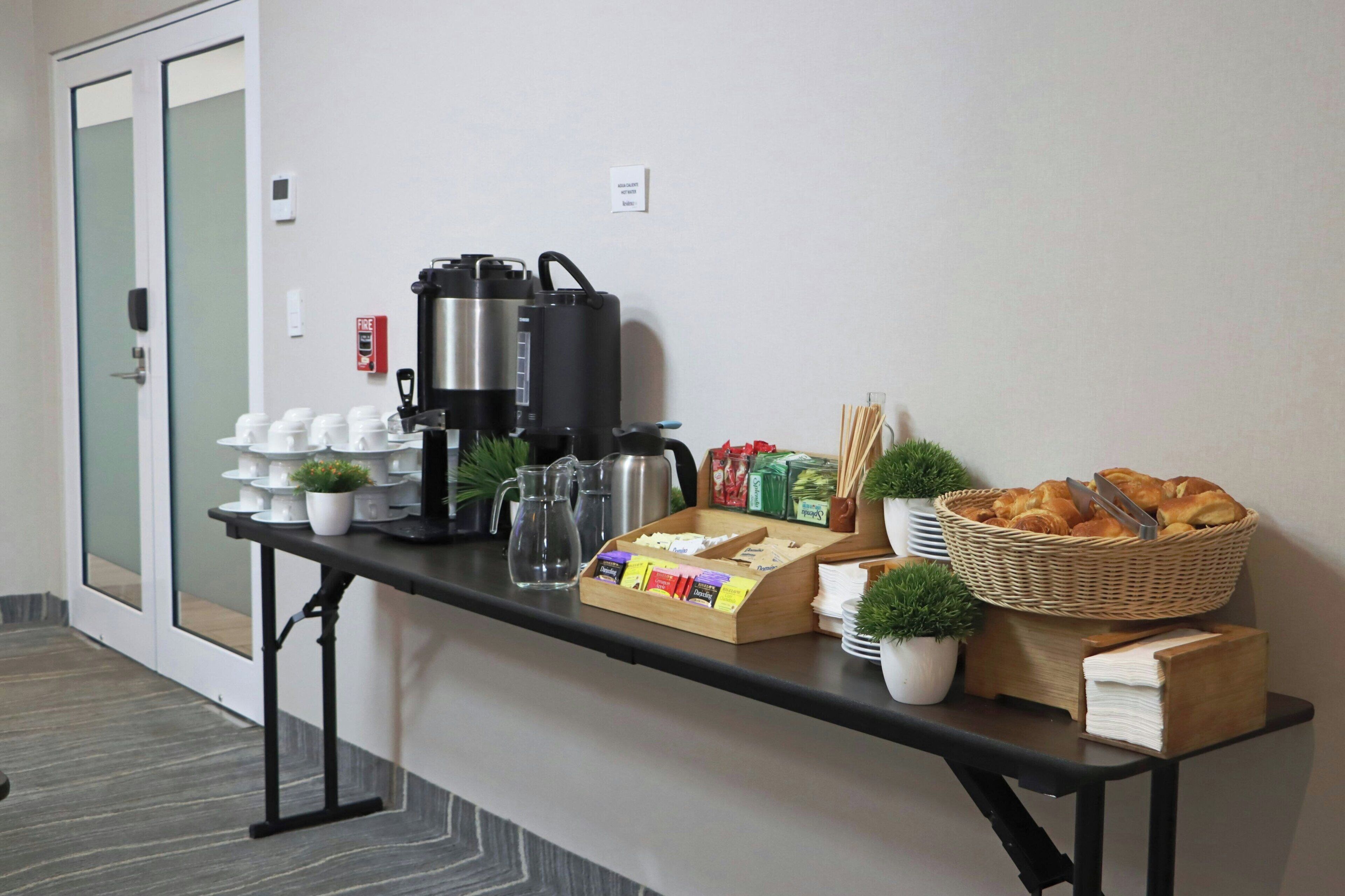 Una mesa de buffet con cafeteras, un espacio para café y una cesta de pasteles.