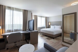 Habitación de hotel con cama, escritorio con silla, televisor y una mesita.