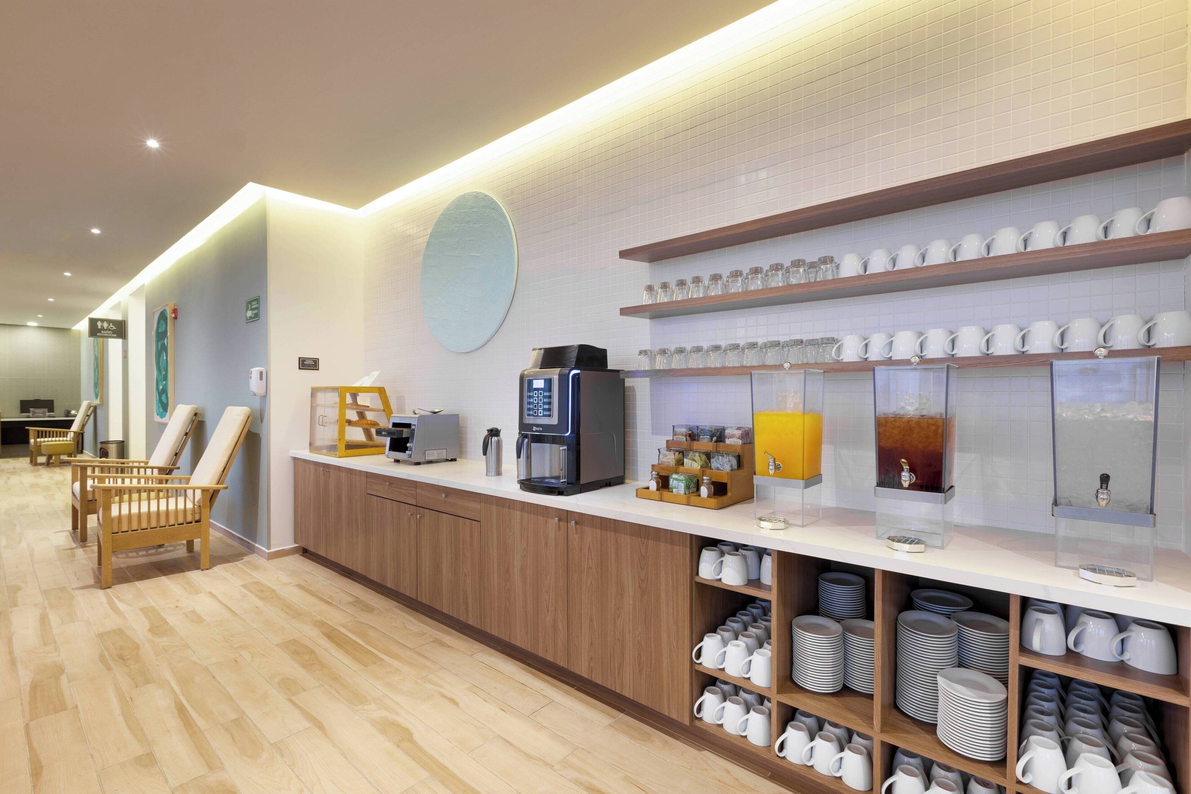 Eine moderne Hotelhalle mit einer Rezeption, einer Lounge und verschiedenen Annehmlichkeiten, darunter eine Kaffeemaschine, eine Teeausgabe und eine Auswahl an Tassen und Tellern.