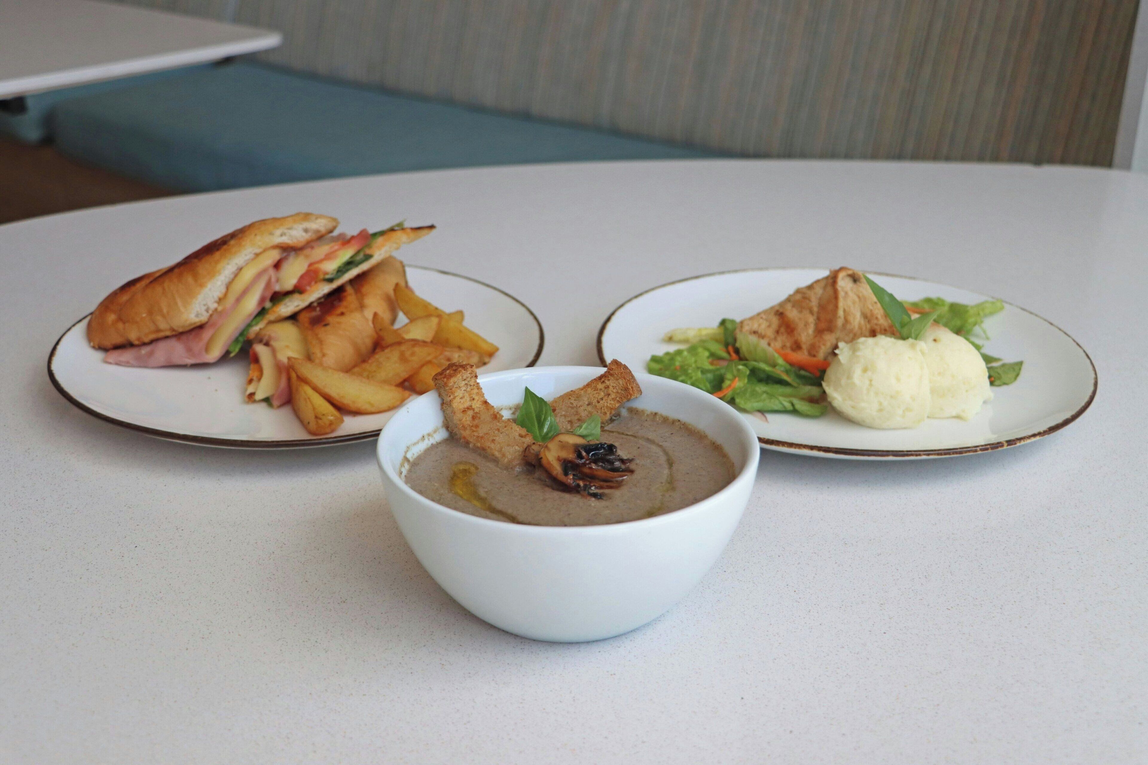 Ein Tisch mit drei Speisen: einem Sandwich, Pommes und einem Salat mit einer Kugel Eis.