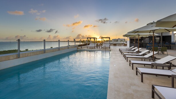 A poolside area with lounge chairs and umbrellas, overlooking a body of water during sunset. - Residence Inn by Marriott Cancun Hotel Zone (Cancun)