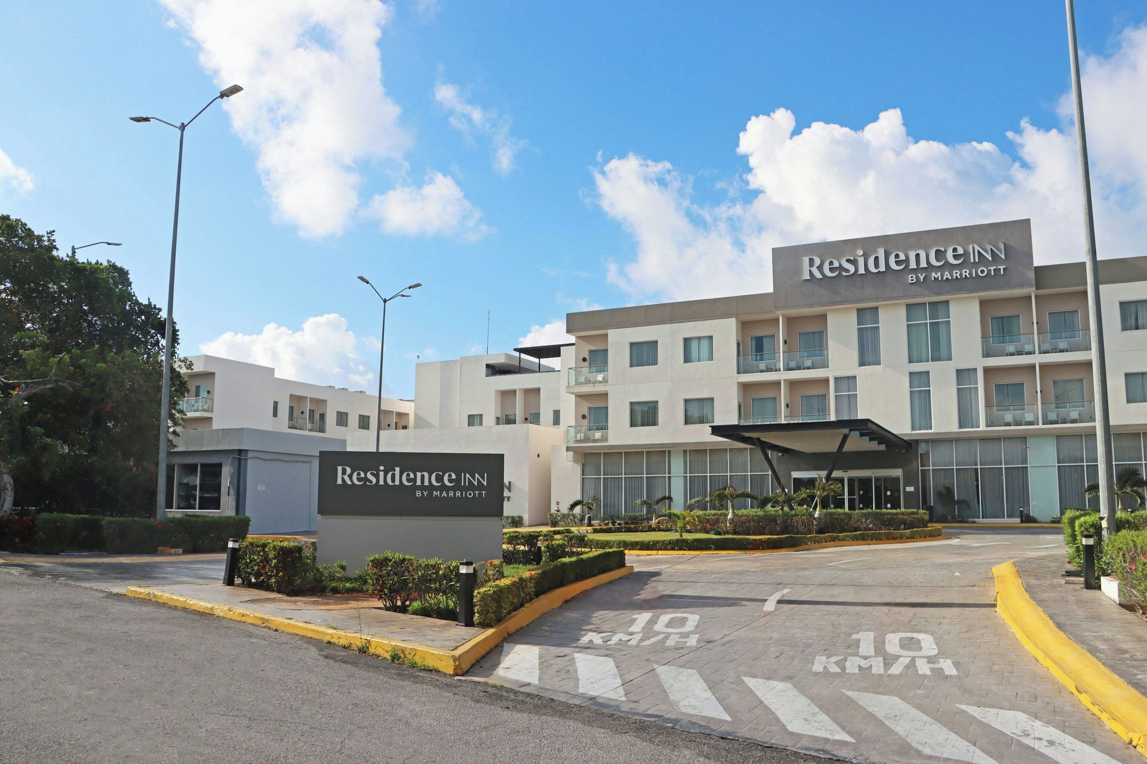 Ingresso moderno di un hotel con una segnaletica che riporta 'Residence Inn by Marriott', una pensilina e un cartello stradale che indica un limite di velocità di 10 km/h.