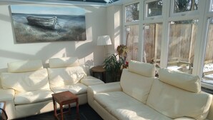 Ein sonnendurchflutetes Wohnzimmer mit einem beigen Sofa, einem kleinen Holztisch und einem Gemälde eines Bootes an der Wand.