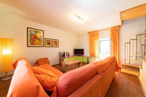 A modern living room with orange furniture, a flat-screen TV, a table, and a staircase. - Villa Providenca in Kastel Stari (Kaštel Stari)