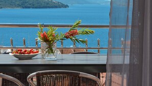 Een balkon met een tafel, rieten stoelen, een schaal aardbeien en een vaas met bloemen.