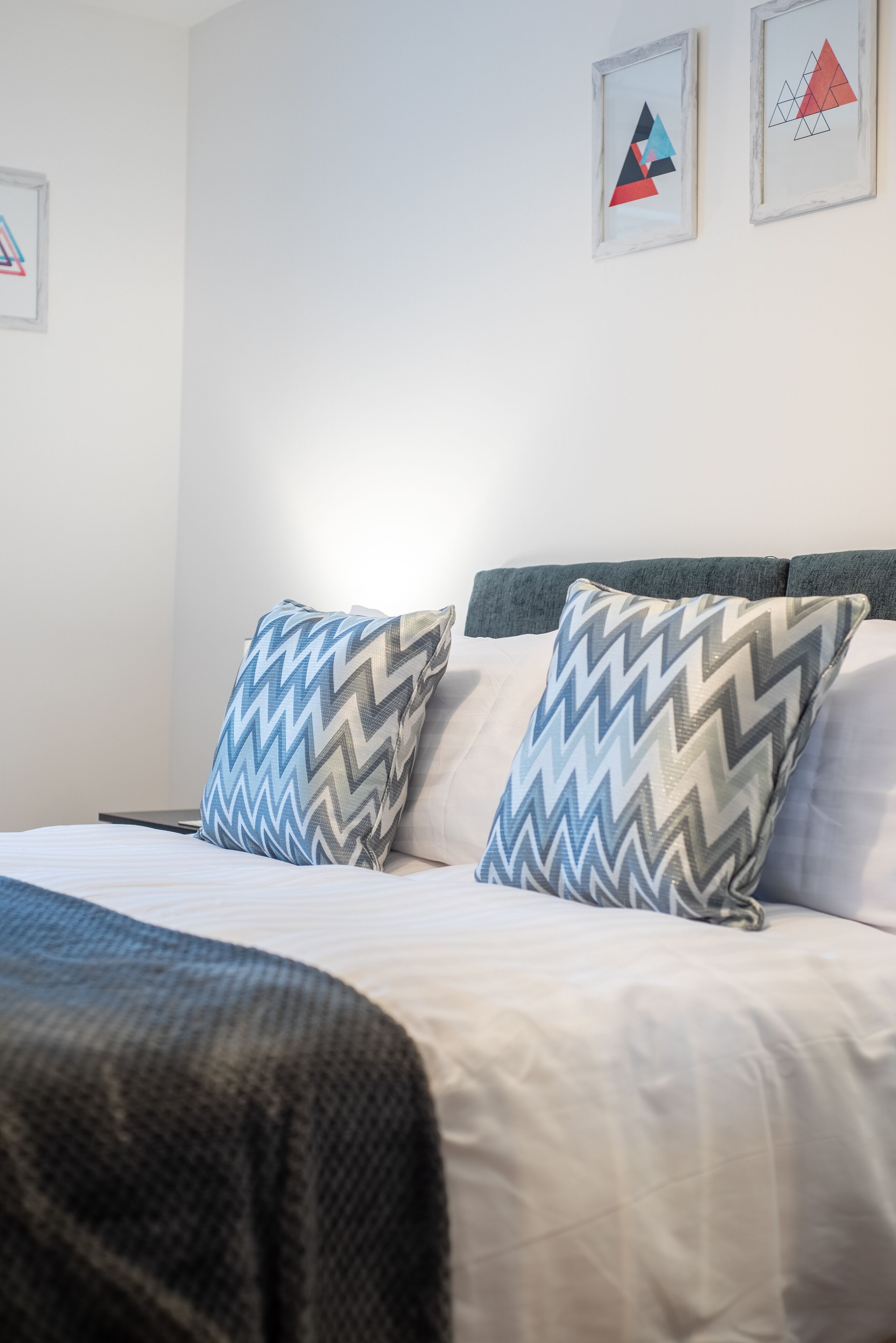 Una cama bien hecha con almohadones estampados y una pared lisa con dos cuadros enmarcados.