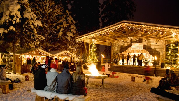 A snow-covered outdoor area with wooden benches and a covered stage with lights. - Description (Schwendau)