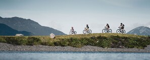 A group of cyclists on a grassy hill with a lake and mountains in the background. - Description (Schwendau)
