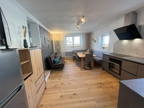 A modern kitchen with a dining area, wooden flooring, and a built-in oven. - Description (Schwendau)