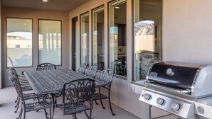 Une terrasse extérieure avec une table et des chaises en métal, un barbecue et de grandes fenêtres offrant une vue sur le paysage environnant.