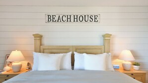 A neatly made bed with white linens, two bedside tables with lamps, and a sign above the bed that reads "BEACH HOUSE". - Sam's Cove! Second Floor Condo Overlooking Water (Holmes Beach)