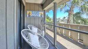 A balcony with two white wicker chairs, a sign reading "Sam's Cove Holmes Beach FL", and a view of palm trees and beach. - Sam's Cove! Second Floor Condo Overlooking Water (Holmes Beach)