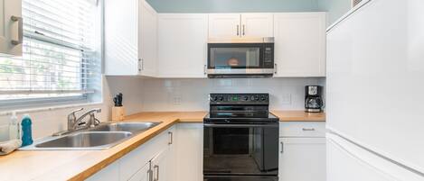 A compact kitchen with white cabinets, a stainless steel microwave, a black oven, and a wooden countertop.