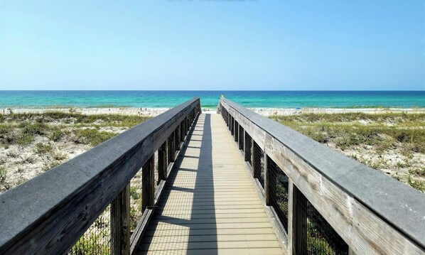 Une promenade en bois menant à une plage, avec un ciel dégagé.