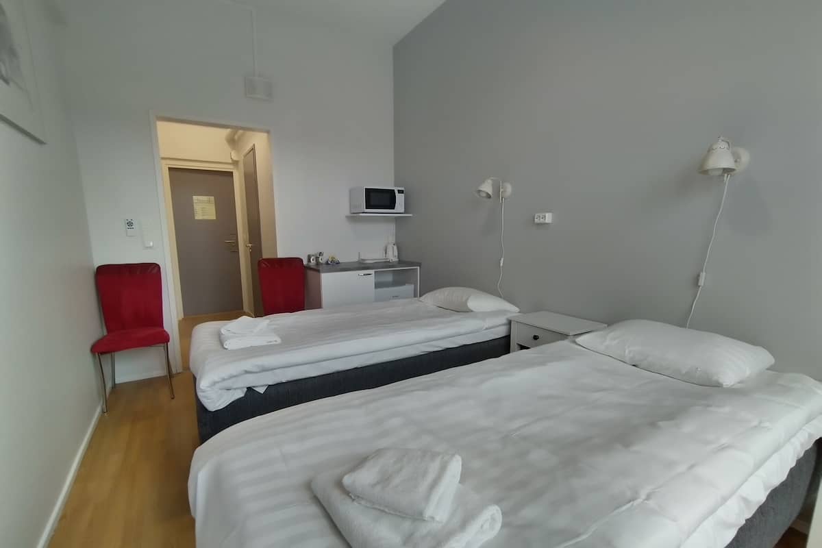 Habitación de hotel con dos camas, un escritorio con silla, microondas y una silla roja.