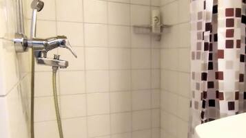 Un baño pequeño con azulejos, ducha, inodoro y lavamanos.