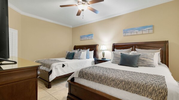 A hotel room with two beds, a ceiling fan, a TV, and artwork on the walls.