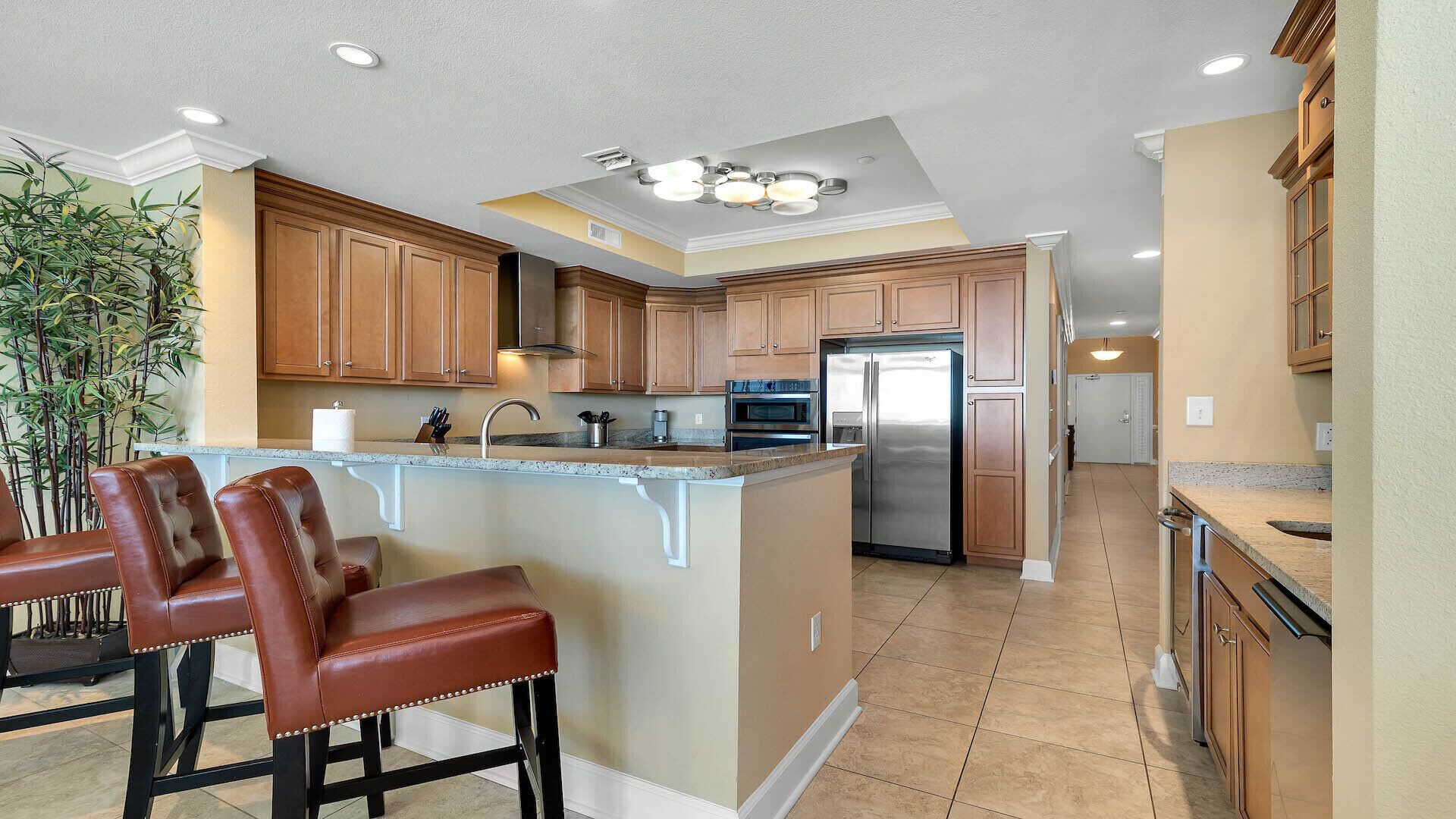 A spacious kitchen with a central island, wooden cabinets, stainless steel appliances, and a seating area with leather chairs.