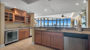 A modern kitchen with wooden cabinets, a stainless steel dishwasher, and a large island with a sink. - Parking level!  Lazy river/Slide. New to the rental market!! (Orange Beach)