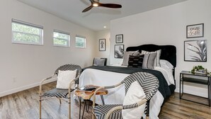 Une chambre à coucher comprenant un lit, deux chaises, une petite table, une table de chevet et un ventilateur de plafond.