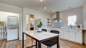 Une cuisine moderne avec des meubles blancs, un plan de travail en marbre, une chaise noire en osier et un luminaire suspendu au plafond.
