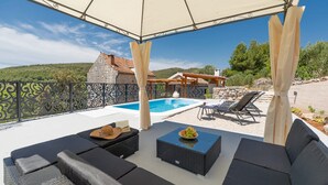 Ein überdachter Außenbereich mit Pool, Liegestühlen und einem Gebäude im Hintergrund.