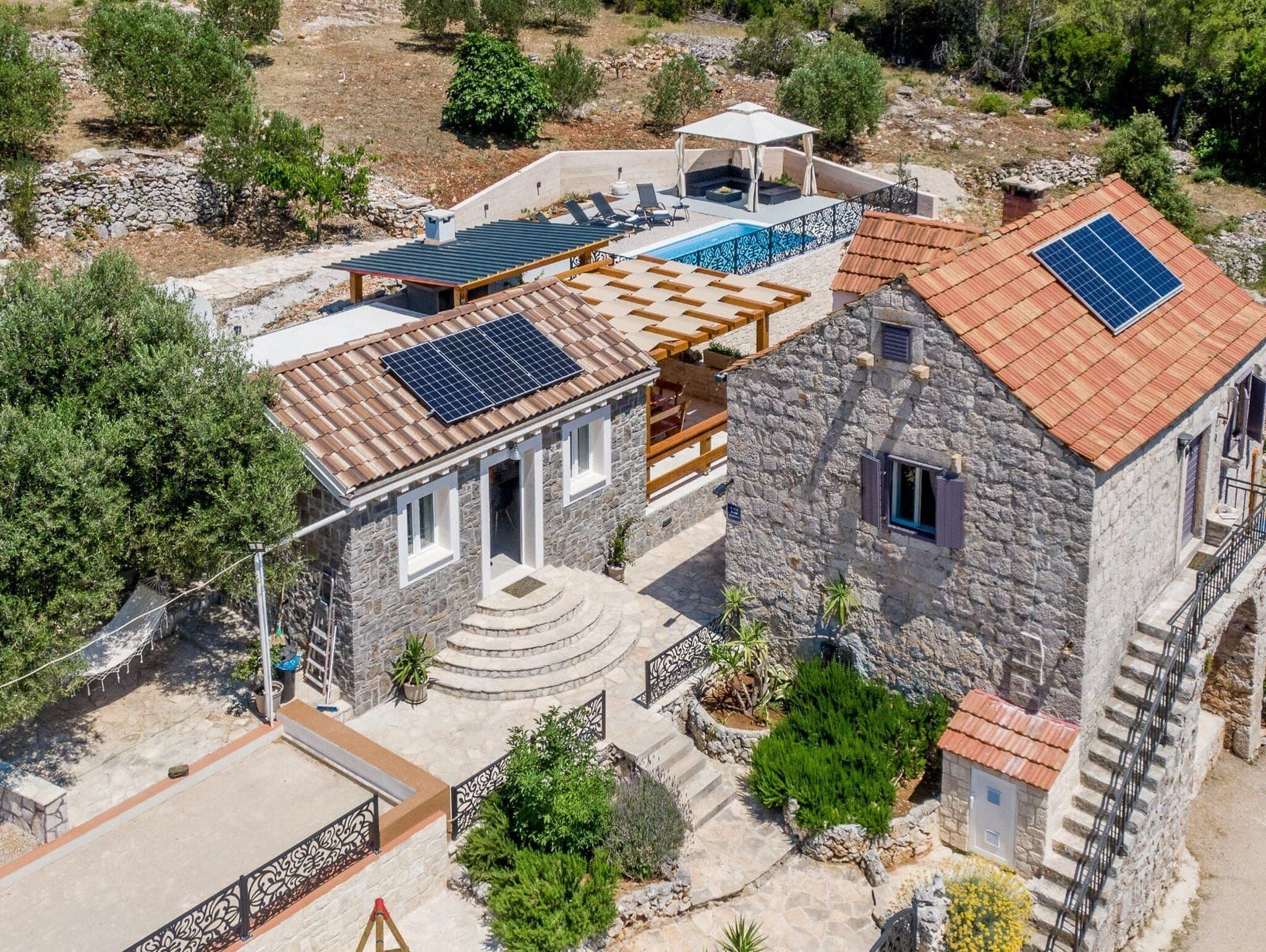 Uma casa de pedra com piscina, painéis solares e um alpendre coberto.