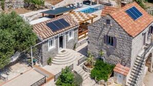 Ein Steinhaus mit Pool, Solaranlage und überdachter Terrasse.