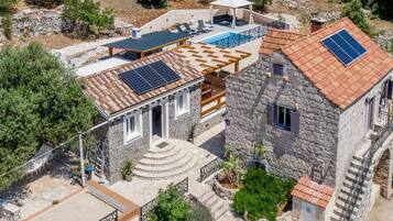 Uma casa de pedra com piscina, painéis solares e um alpendre coberto.