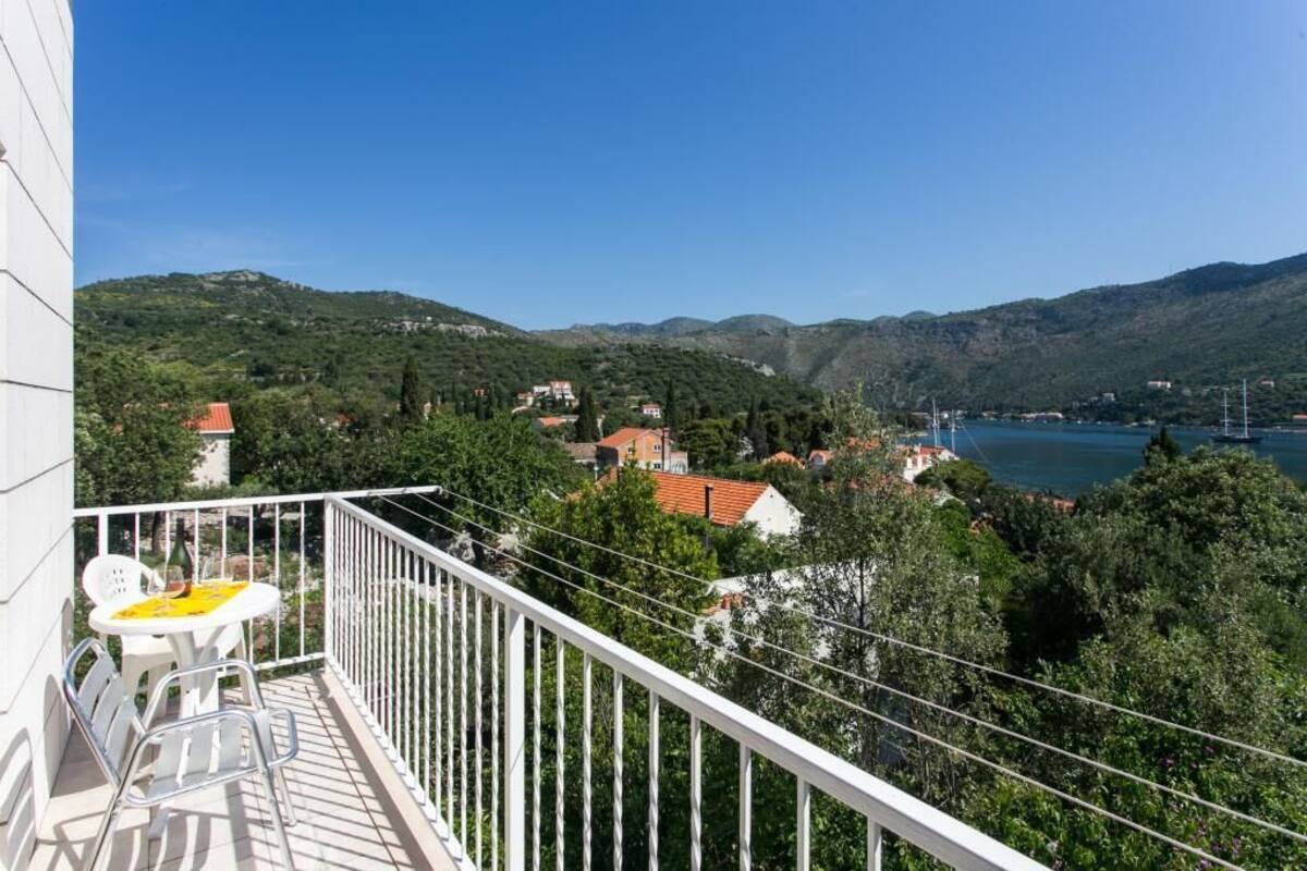 A balcony with a table and chairs, overlooking a lake with boats and houses in the background.