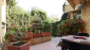 Un espace patio aménagé avec une table et des chaises, entouré de plantes en pot et d’un mur en briques.