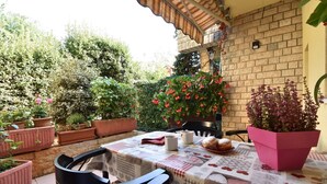 Une terrasse extérieure avec une table dressée pour deux personnes, entourée de plantes en pot et d’un mur de briques.
