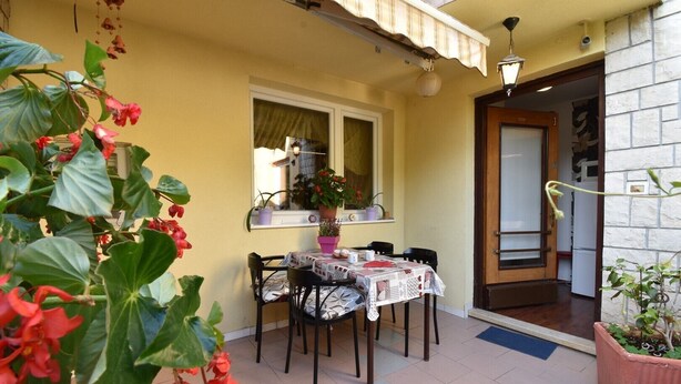 Une petite terrasse avec une table et des chaises, une fenêtre donnant sur un beau paysage et des plantes en pot.