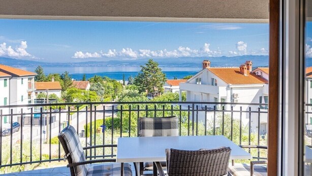 Een balkon met een tafel en stoelen, met uitzicht op de kust, huizen en een heldere lucht.