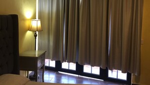 A room with a bed, a nightstand with a lamp, and a window with curtains.