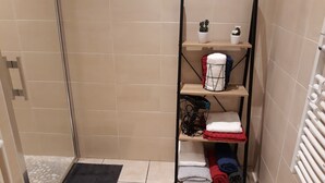 Une salle de bain équipée d’une douche, d’un porte-serviettes, d’une étagère pour les articles de toilette et d’un radiateur.