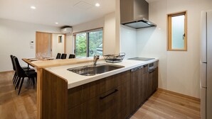 A modern kitchen with a wooden island, stainless steel appliances, and a large window providing natural light. - Villars Chalet (Hakuba)
